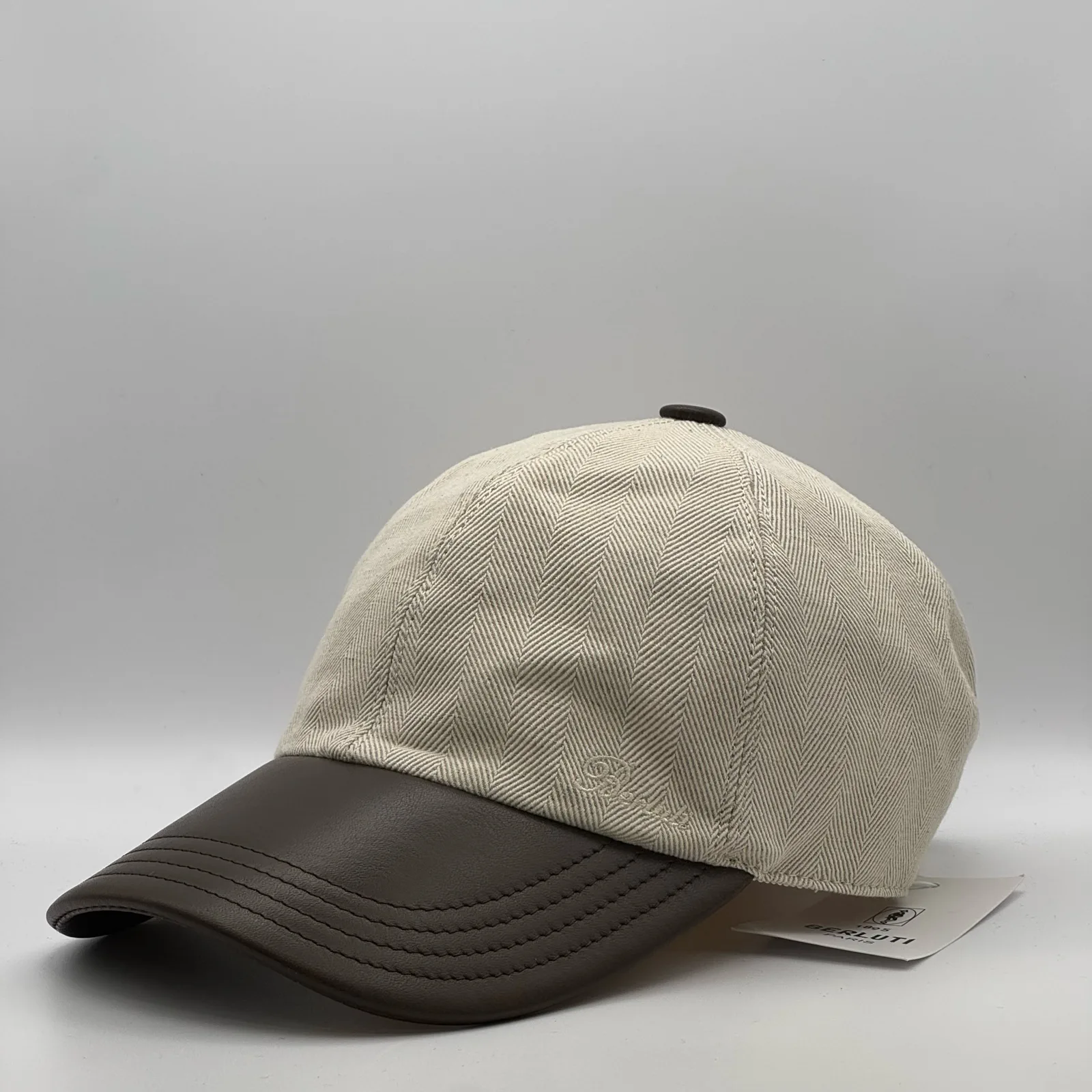 Berluti linen cap, side profile in herringbone linen with a dark brown leather brim.