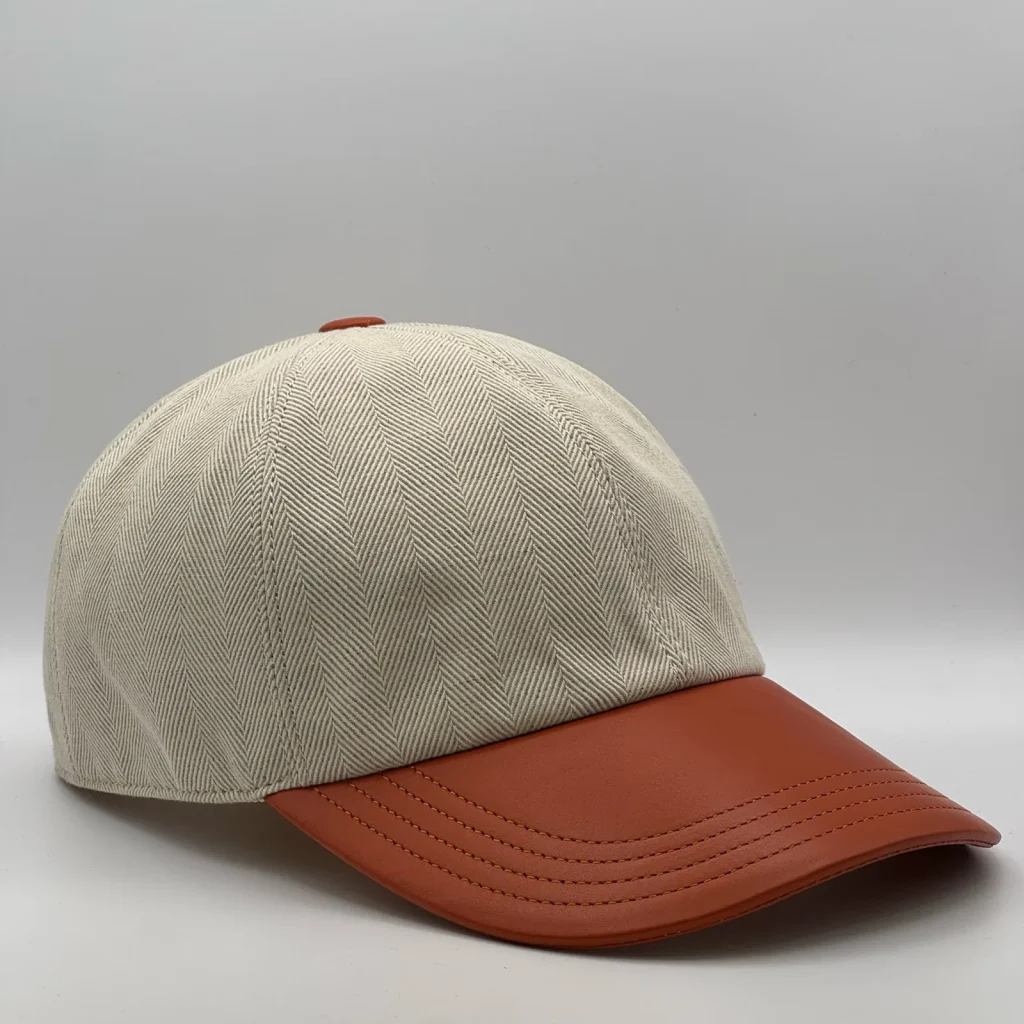 Berluti linen cap, three-quarter view showing the tan leather brim and tonal button.