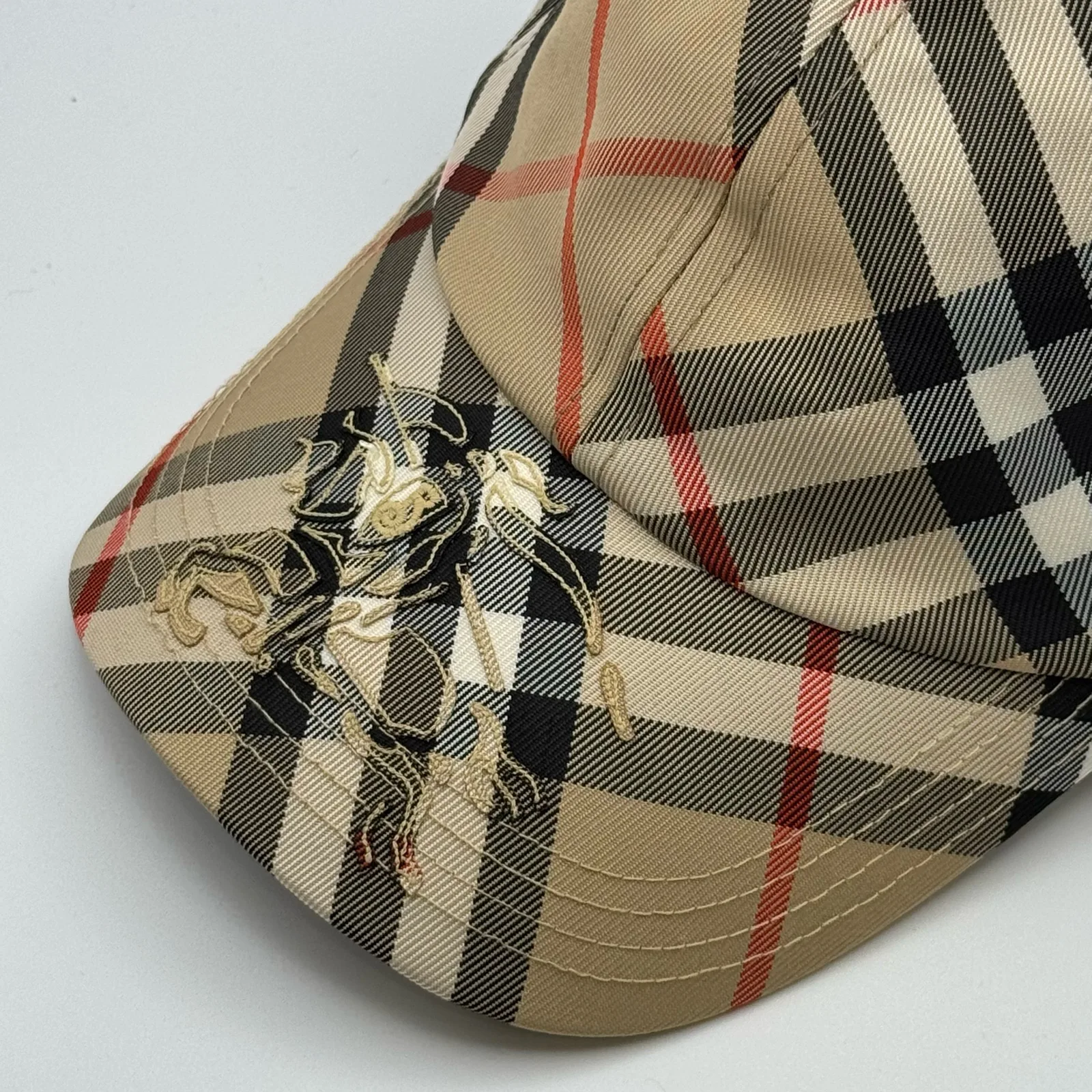 Close-up of the equestrian knight design embroidered on the brim of the beige check cap.