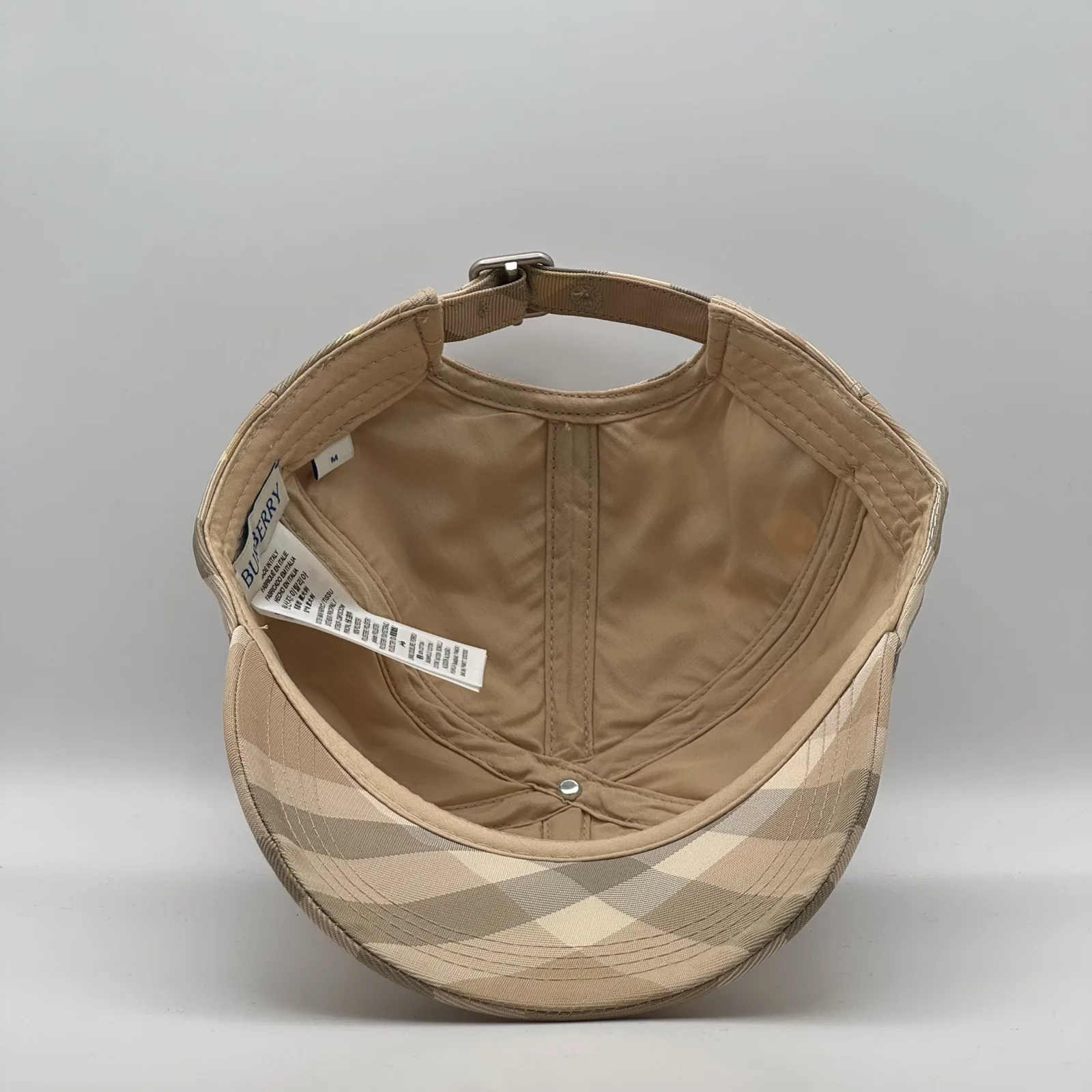 Underside of the pale beige check cap, brim lifted to show the interior.
