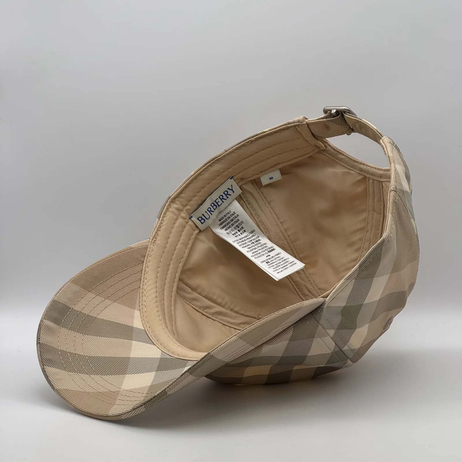Close-up of the care label and interior tag inside the pale beige check cap.