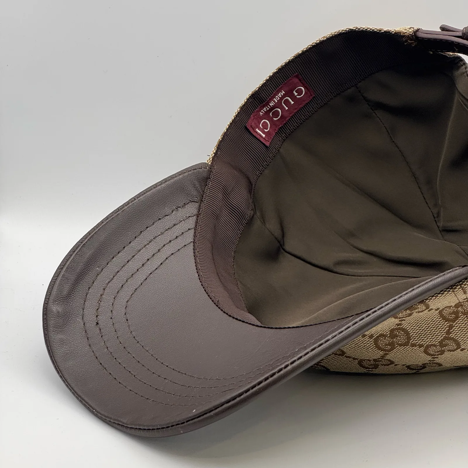 Beige GG canvas cap, brim lifted showing the dark leather underside and tag