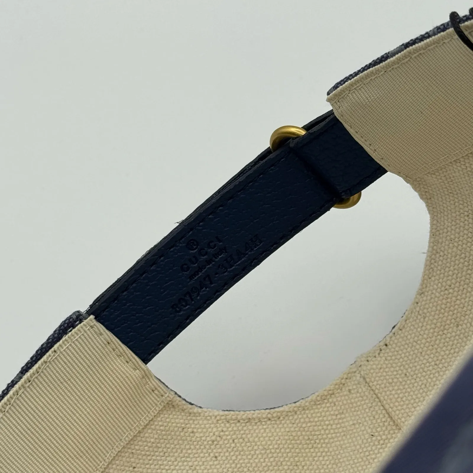 Denim blue GG canvas cap, close-up of the cream leather strap and gold grommet