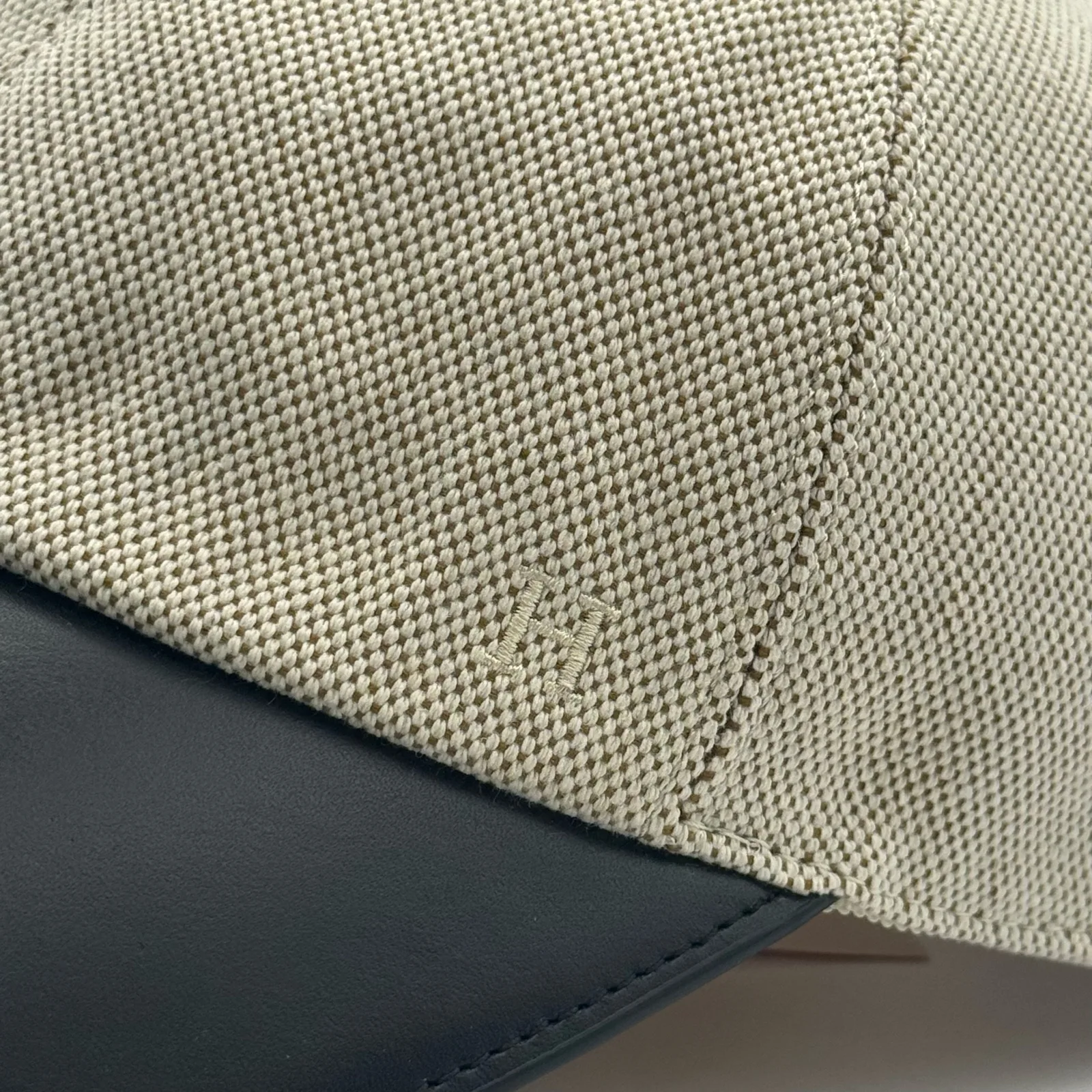Close-up of the black leather brim meeting the woven canvas crown, with a small tone-on-tone logo.