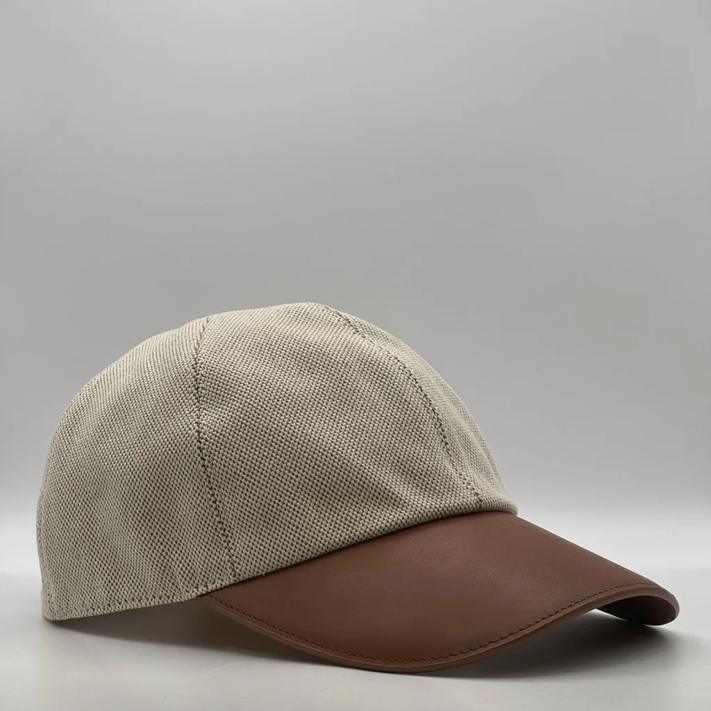 Hermès canvas cap, three-quarter view showing the brown leather brim and tonal button.
