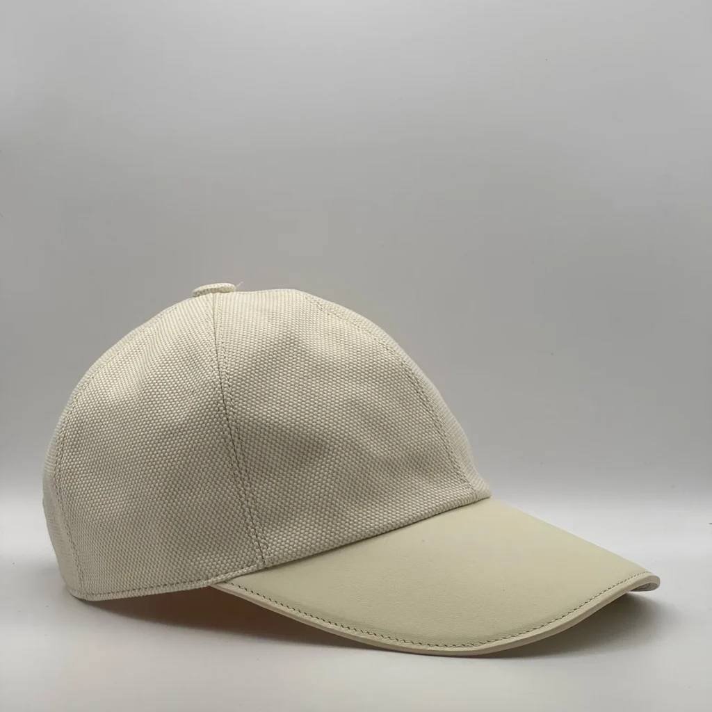 Hermès canvas cap, three-quarter view showing the cream leather brim and tonal button.