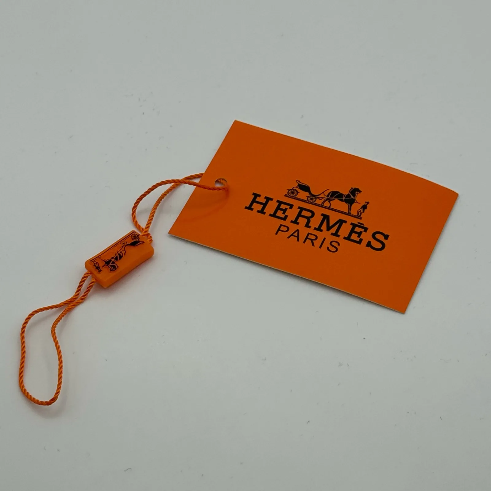 Hermès branded gift tag and ribbon photographed alongside the cap.