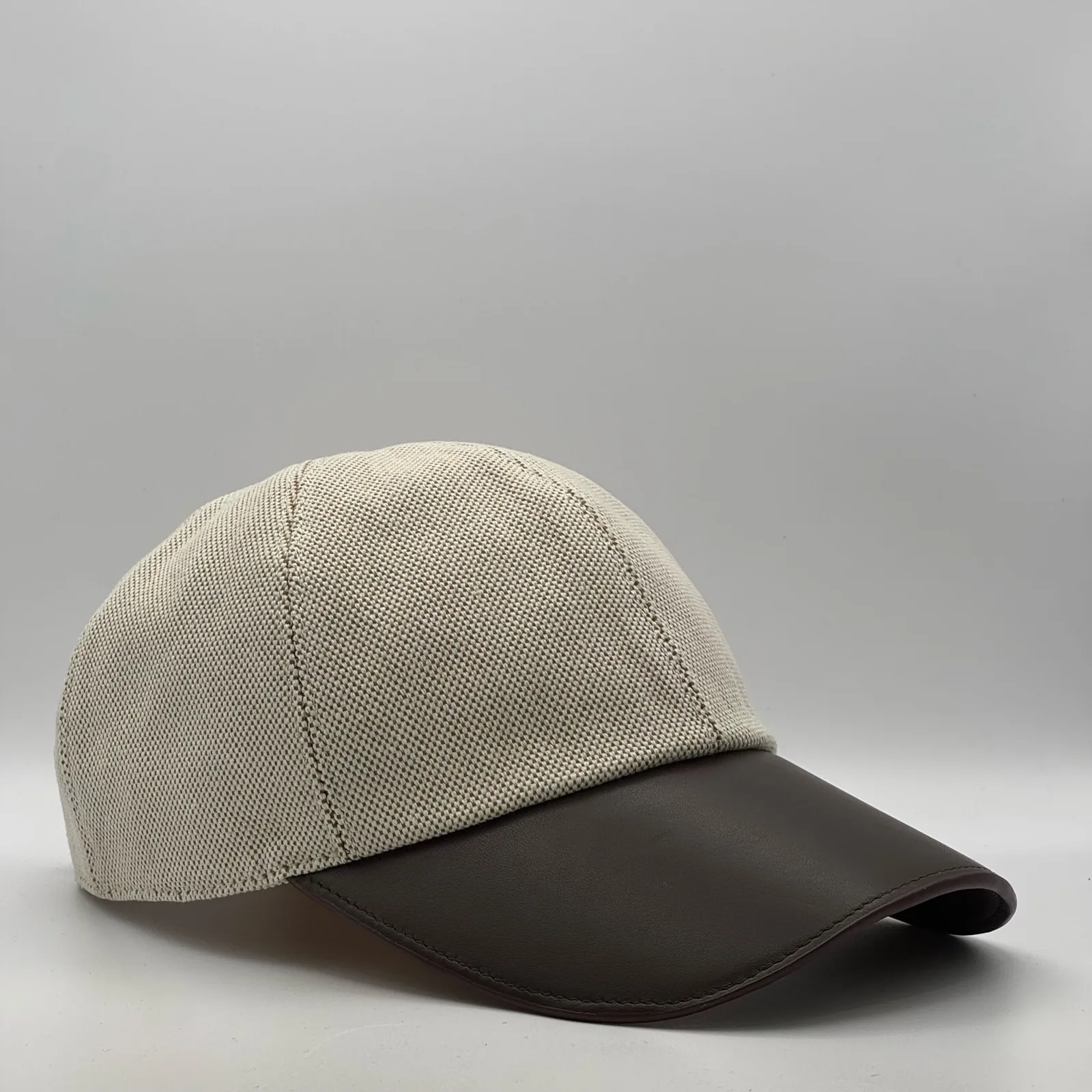 Hermès canvas cap, three-quarter view showing the dark brown leather brim and tonal button.