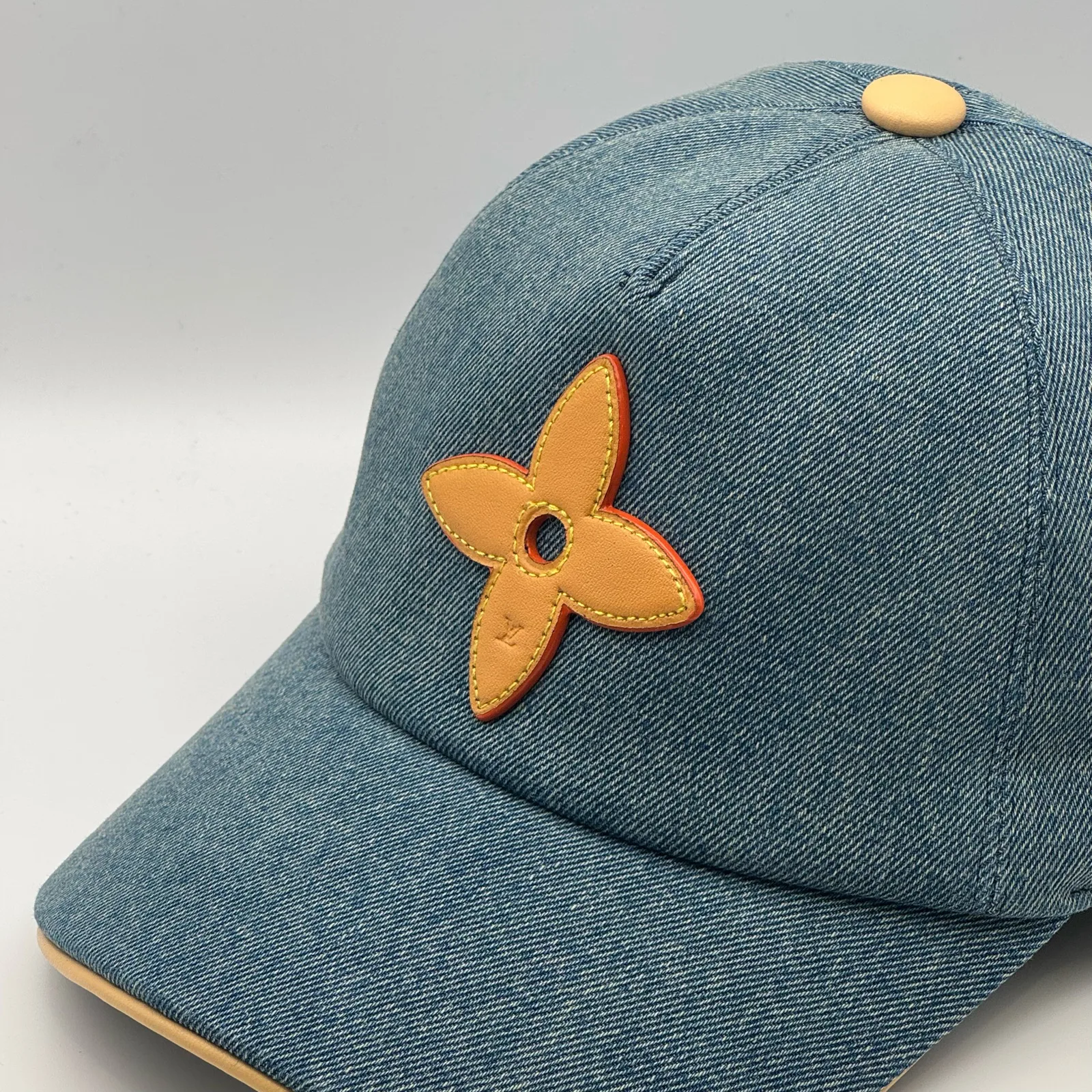 Close-up of the tan leather flower emblem on the blue denim cap.