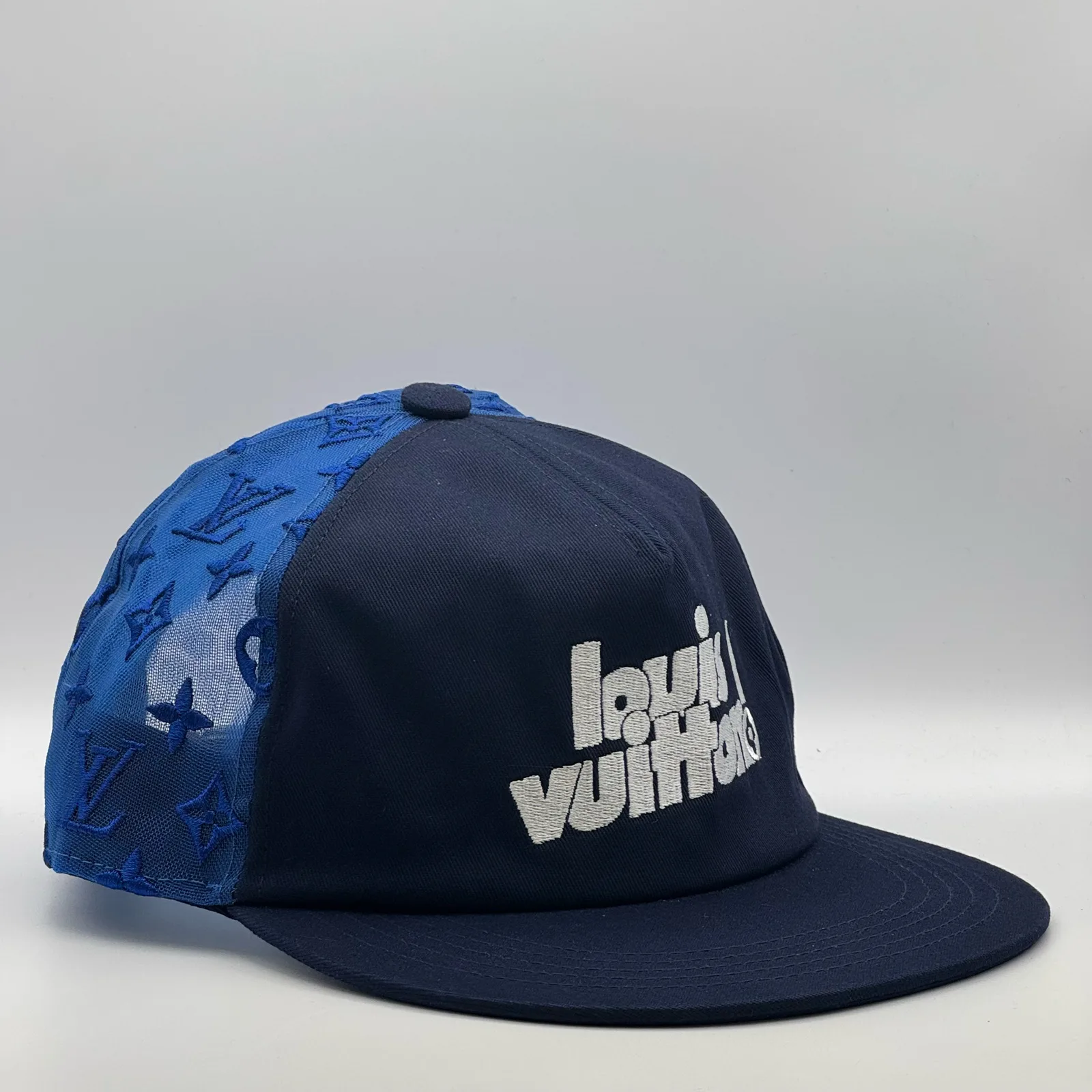 Navy logo mesh cap, three-quarter side view showing the blue monogram mesh panel.