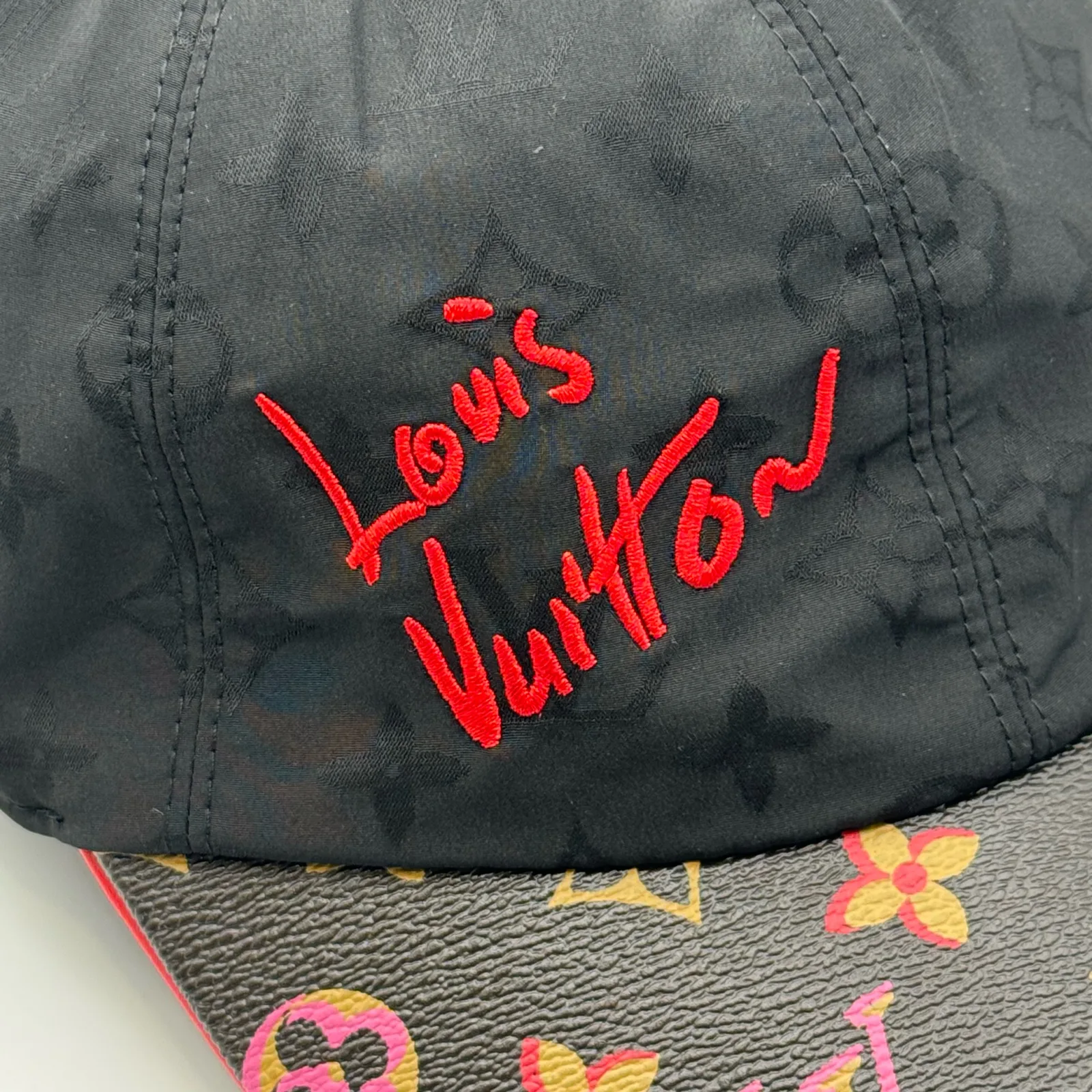 Close-up of the red script logo above the monogram canvas brim.